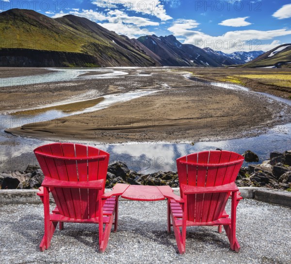 Multi-colored mountains from mineral rhyolite are lit with sun. Two red chaise lounges stand for tourists