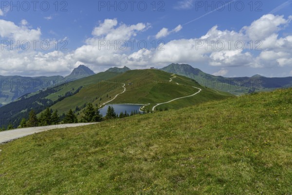 Hilly mountain landscape with hiking trail and small lake under a blue sky, mittersill, hohe tauern, austria