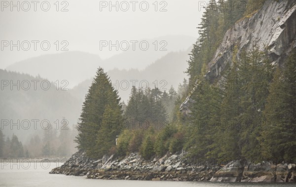 Misty forested mountains and rocky coastline bordering a calm body of water along the Sea to Sky Highway in British Columbia, Canada, North America