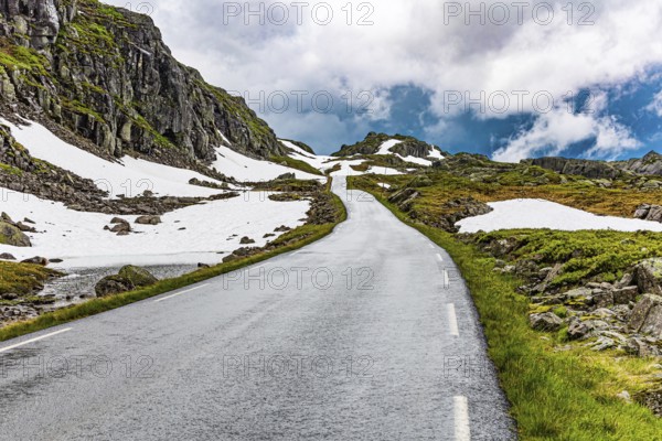 Narrow dangerous mountain road glitters from the rain. Traveling by camper on road 520. Gray rocks surround the lake. Summer in Norway