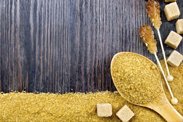 Sugar brown granules in a spoon, cubes and crystals on a stick in the form of a frame on the background of a wooden board