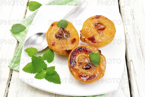 Three halves of quince baked with honey, mint and spoon in a plate on a napkin against a light wooden board