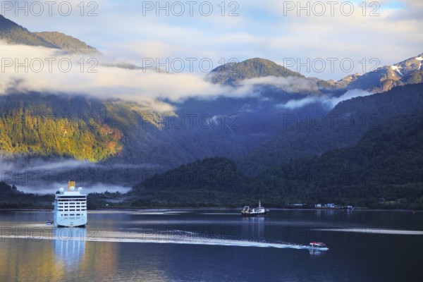 Snow-white tourist boat lit rising sun. On the mountains are thin clouds. Sunrise in the Chilean fjord