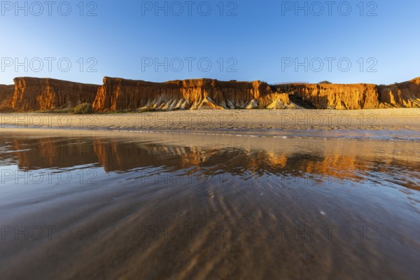 A landscape on the beach at low tide. The surrounding rocks and cliffs are reflected in the sea at sunset. Praia da Falésia, Algarve, Portugal, Europe