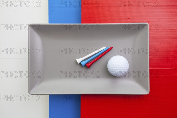 Gray ceramic dish with golf equipments on over white, blue and red wooden table, rectangle dish