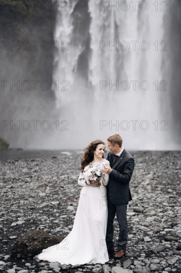 Wedding couple near Skogafoss waterfall. Destination Iceland wedding. The groom hugs the bride by the shoulders, they laugh together