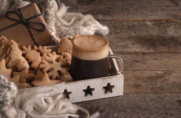 Christmas breakfast table with a tray full of gingerbread cookies, a cup of coffee, a wool scarf, and a gift, on a vintage wooden table