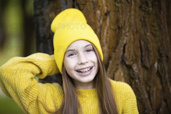 Portrait of modern happy teenage girl with braces dressed in yellow clothes in park. Pretty teenage girl with braces smiling happily. Kid girl in autumn smiling with braces teeth device