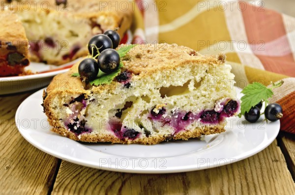 Sweet piece of cake with black currant on a plate, napkin on the background of wooden boards