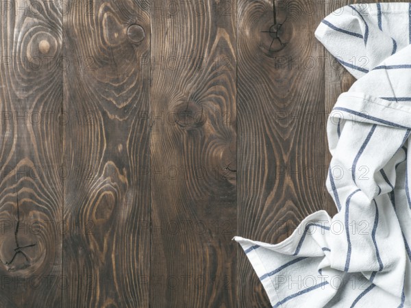 View from above on brown wooden table with linen kitchen towel or textile napkin. Blue tablecloth on dark brown wood tabletop. Copy space for text. Can use as mock up for design