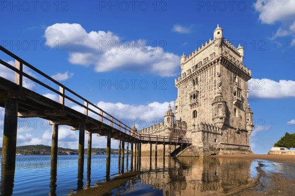 Belem tower and wooden bridge to it, Lisbon, Portugal at blue summer day sky with clouds. Medieval fort on Tagus river in late Gothic or Manueline style, UNESCO world heritage site, Age of Discoveries, tourist attraction, Portuguese seafaring history