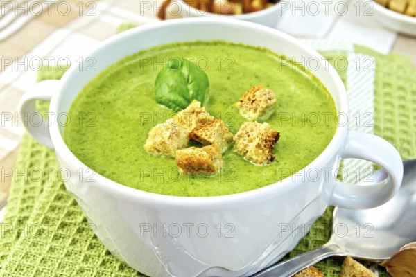 Green soup puree in a white bowl with croutons and spinach leaves on a napkin on the background fabric