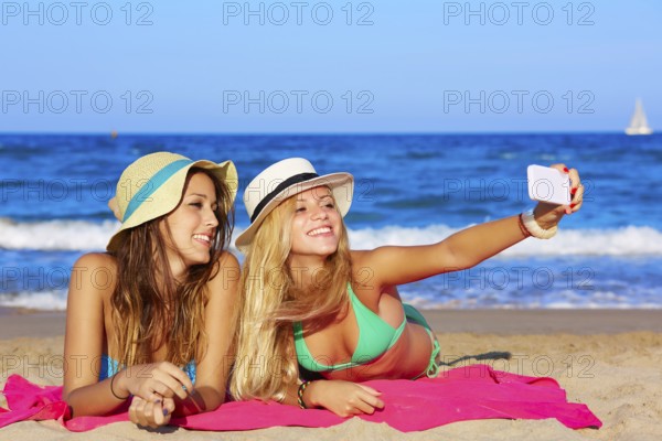 Happy girl friends selfie portrait lying on beach sand in summer vacation