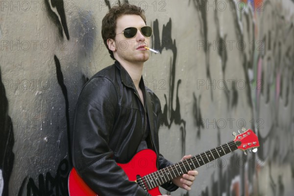 Smoking cigarette rock leather boy playing guitar outdoor on silver wall backgorund