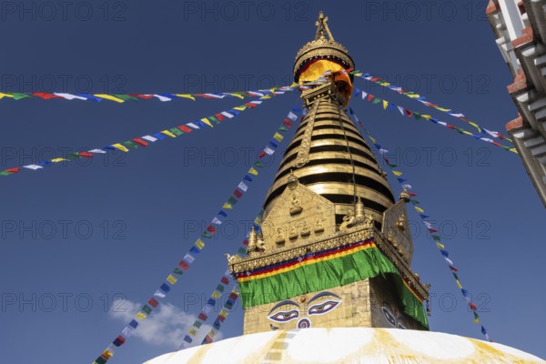 Swayambhunath, Swayambhu Mahachaitya, sometimes called the Monkey Temple, the Swayambhu stupa, one of the UNESCO World Heritage Sites of the Kathmandu Valley photographed in winter against the blue sky. On the white dome, with a pigeon walking on it, stands a cubic part, the harmika, with eyes painted on its four sides, known as Eyes of Buddha or Wisdom Eyes. The golden spire is above it, and Buddhist prayer flags hang from the top. Kathmandu Metropolitan City, Bagmati Province, Nepal, Asia