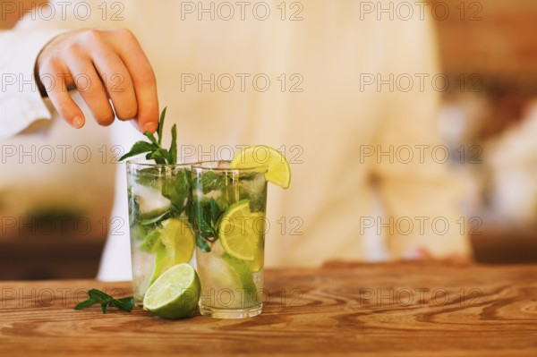 Bartender making two mojito cocktails on wooden bar counter