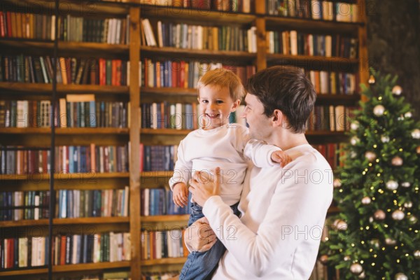Happy young father and son have fun playing at home near Christmas tree. New Year and Christmas theme. Festive mood. Family winter holiday concept. Dad and son in their arms in the evening near fir tree
