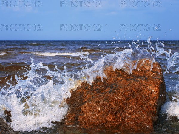 Water splashes over the red rocks against blue sky
