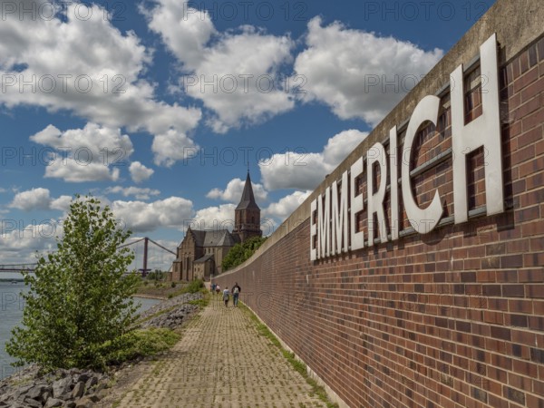 Brick wall and sign of Emmerich, next to it a path along the river on a sunny day, emmerich, lower rhine, germany