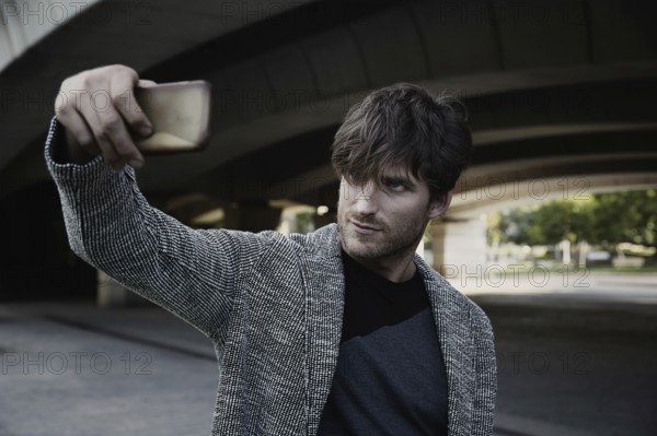 Modern young man smartphone taking selfie photos under a bridge