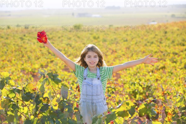 Kid girl in happy autumn vineyard field open arms with red leaf in hand