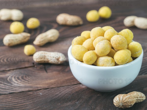 Peanut snack for beer, wine, party bar. Salted peanuts in yellow cheese glaze on brown wooden table. Copy space
