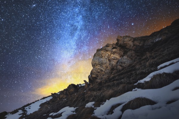 Night scenery done on long exposure. A beautiful Caucasian landscape of red rocks against the background of the cold milky way and a warm yellowish red glow on the horizon behind the rocks. The concept of beautiful Caucasian nature in the bright colors o