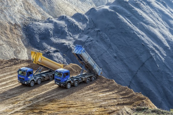 2 dumper trucks stand at the edge of the open-cast mine and tip over a hole