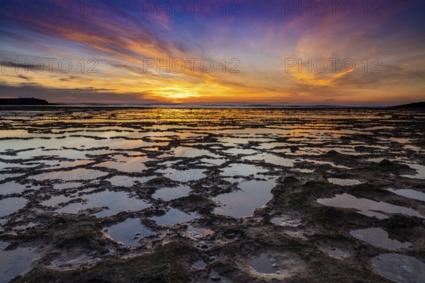 A beautiful sunset over the ocean with rocky beach and tidal pools in the foreground