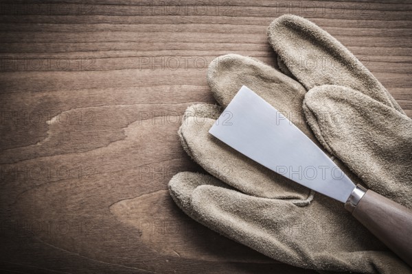 Paint scraper and safety glove on wooden board