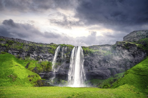 The beautiful Seljalandsfoss waterfall in Iceland surrounded by lava cliffs and green fields in a cloudy sunset