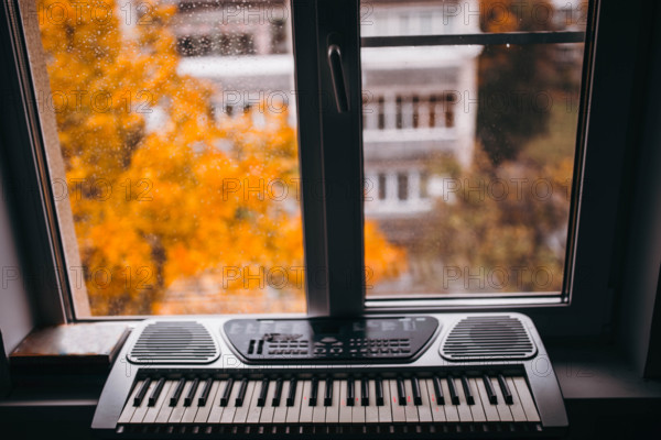 Electronic synthesizer A serene urban view through a window with a keyboard and autumn leaves outside