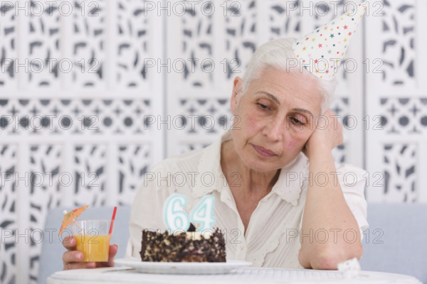 Unhappy elder woman looking her birthday cake holding glass juice hand