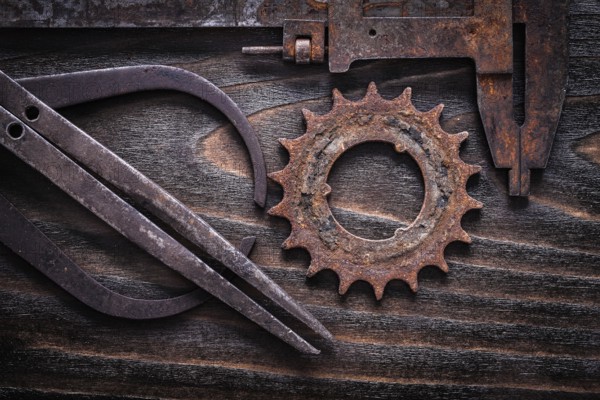 Rusted antique measuring calipers with cog- wheel on vintage dark wooden background close up view construction concept