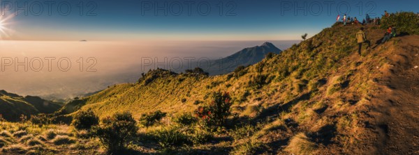 Panoramic photo of mountains surrounding Mount Merbabu and hikers at top during sunrise near Yogya in central Java province in Indonesia. In this region, one can only meet people from isolated local tribes