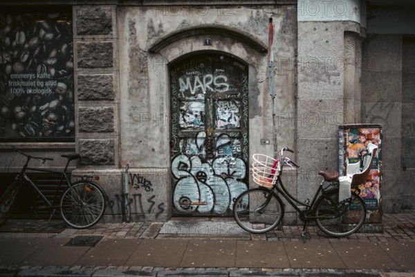 Urban street scene with bicycles and a graffiti-covered door against a weathered brick wall in Copenhagen, Denmark, Europe