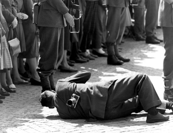 Press photographers. Media is very interested in covering the state visit of Queen Juliana of the Netherlands in Sweden 1957. One male photographer is seen lying on the ground to get an even better view of the event