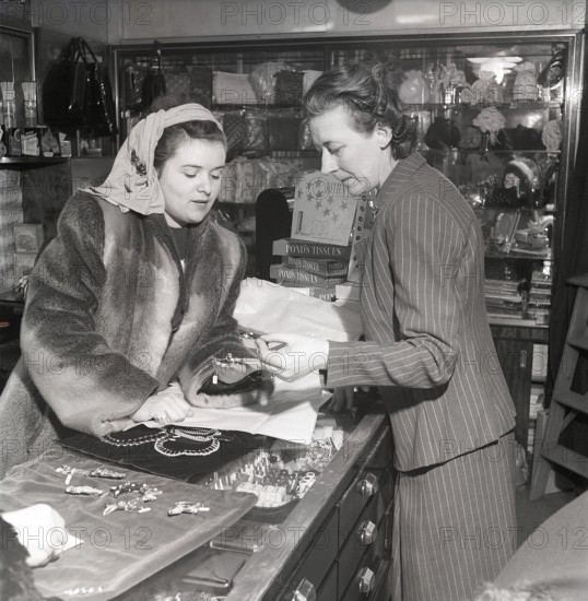 Shopping in the 1940s. A young woman in a store where a sales woman is presenting some of the stores selection of jewellry and charms. On the sales counter products from Pond's tissues is visible. A product marketed as the closest thing to a fine handkerchief, smooth, strong and absorbent. Sweden 1947. Kristoffersson ref AB3-4