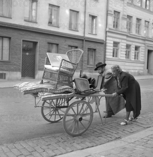 Moving in the 1940s. A couple are pushing a carriage in front of them with some furniture on it. They seem to struggle with it. Sweden 1943. Kristofferson ref C67-4