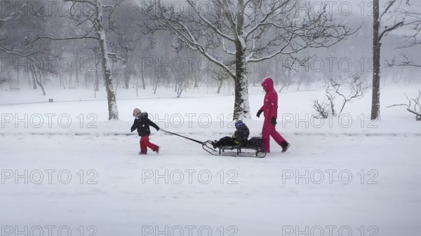 CHISINAU, MOLDOVA - JANUARY 29, 2021 Beautiful scene in the winter park with a mother and child enjoying a sleigh ride. Idyllic and peaceful scene with fluffy snowflakes falling from the sky