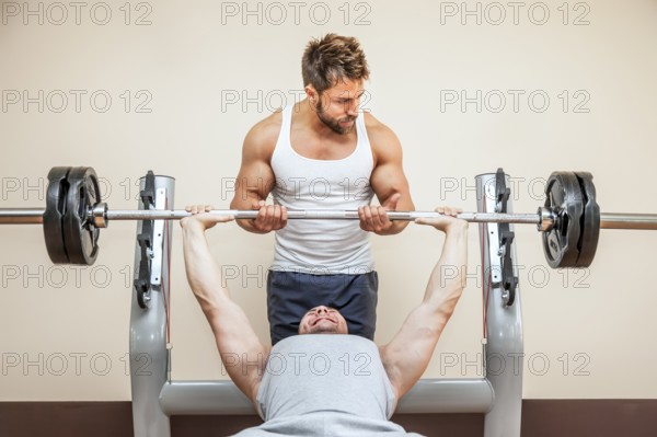 A handsome young muscular sports man doing weight lifting and gets help from his friend