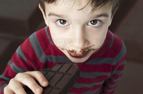 Smiling kid eating chocolate. Smeared stained with chocolate lips
