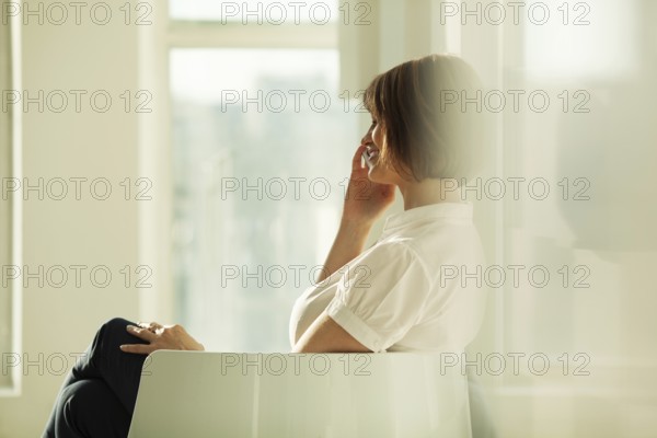 Smiling adult businesswoman talking on smartphone while sitting in chair