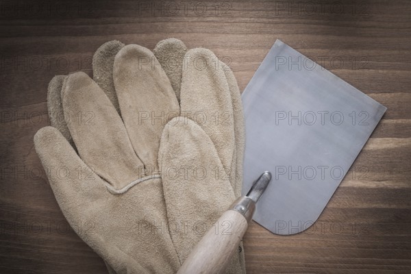 Working safety gloves and bricklaying trowel on vintage wooden background