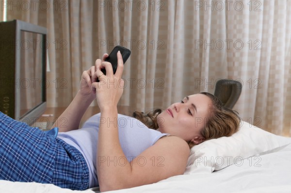 Beautiful young woman texting in bed on her mobile phone