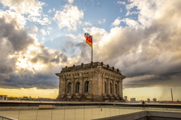 The Berlin Reichstag with evening sky with the flag of Germany and clouds in the background. The Berlin Reichstag with evening sky with the flag of Germany