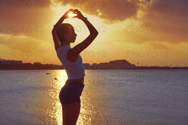 Girl silhouette at sunset heart shape in hands on the beach
