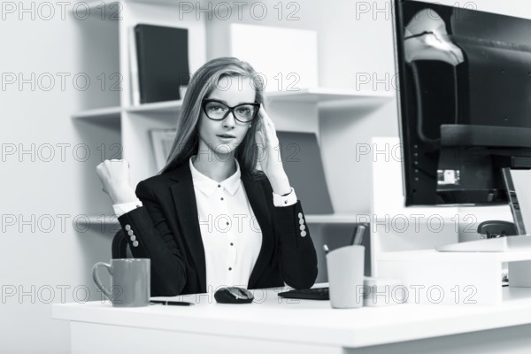Young pretty business woman sitting at the desk with computer in blue office