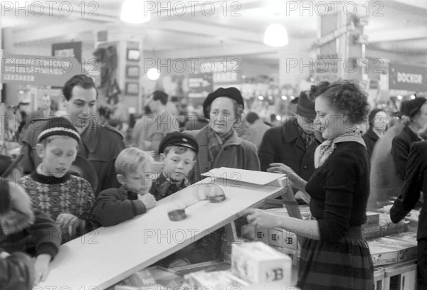 Toys in the 1950s. Interior from the NK department store in Stockholm. A clerk in the toy department shows how the Walking Spring works. A classic toy from the era. The spring was started, for example, on a staircase and then wandered down by itself. The children and adults gathered around the demonstration watch in fascination. Stockholm 1953. Kristoffersson ref 1-2