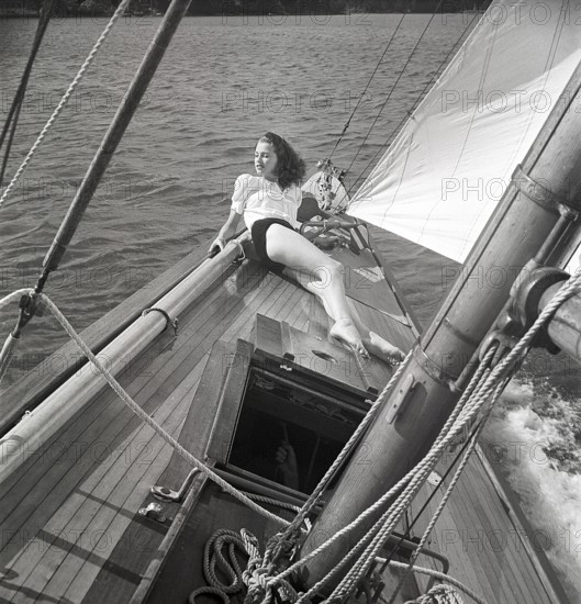 1940s sailing boat. A young woman is aboard a fashionable sailing boat and is lying on deck when it cruises forward with wind in the sails. She is wearing a typical 1940s fashion. Sweden 1946 Photo Kristoffersson ref AC102-2